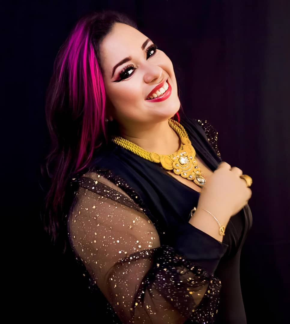 Retrato de Erika “Keka” sonriendo, con vestido negro brillante y collar dorado