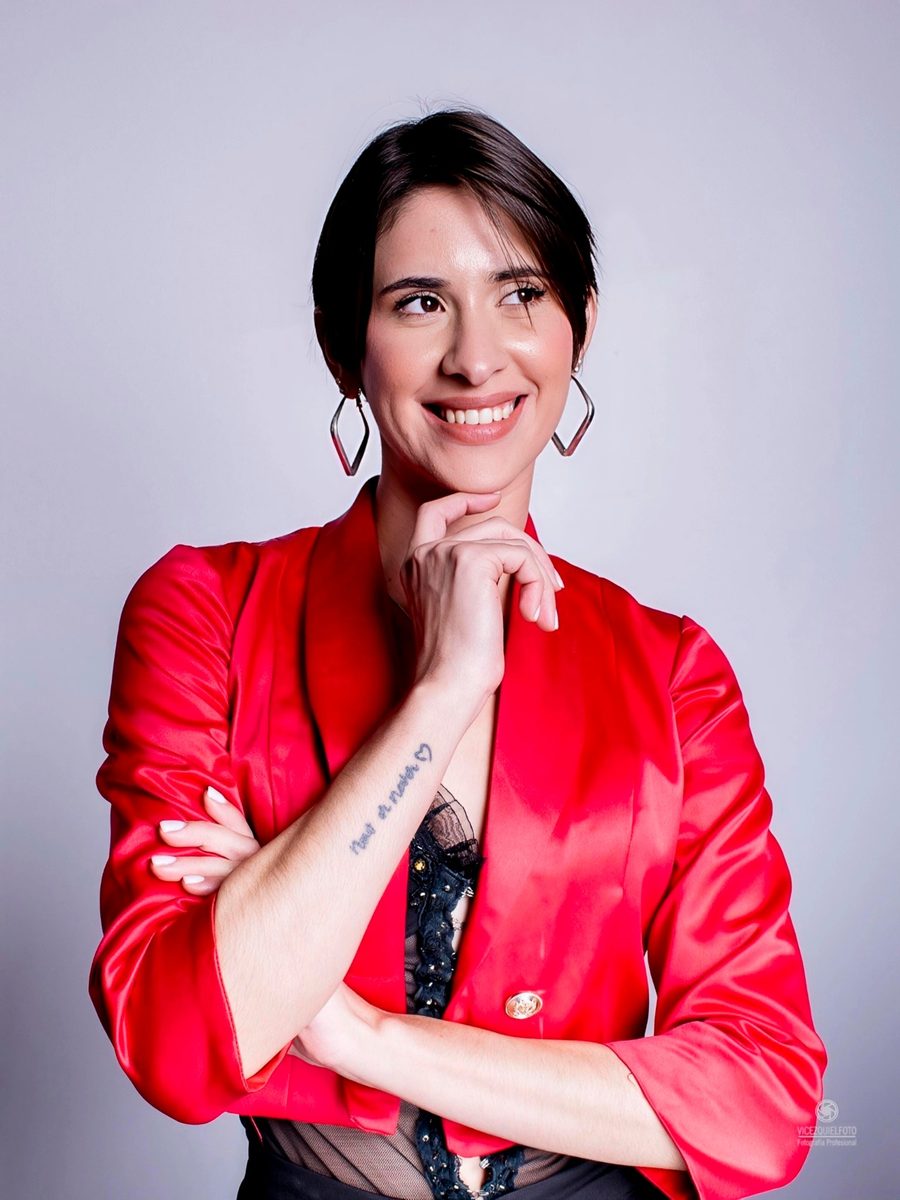 Retrato de Egleidys López con blazer rojo, la mano en el mentón y una sonrisa
